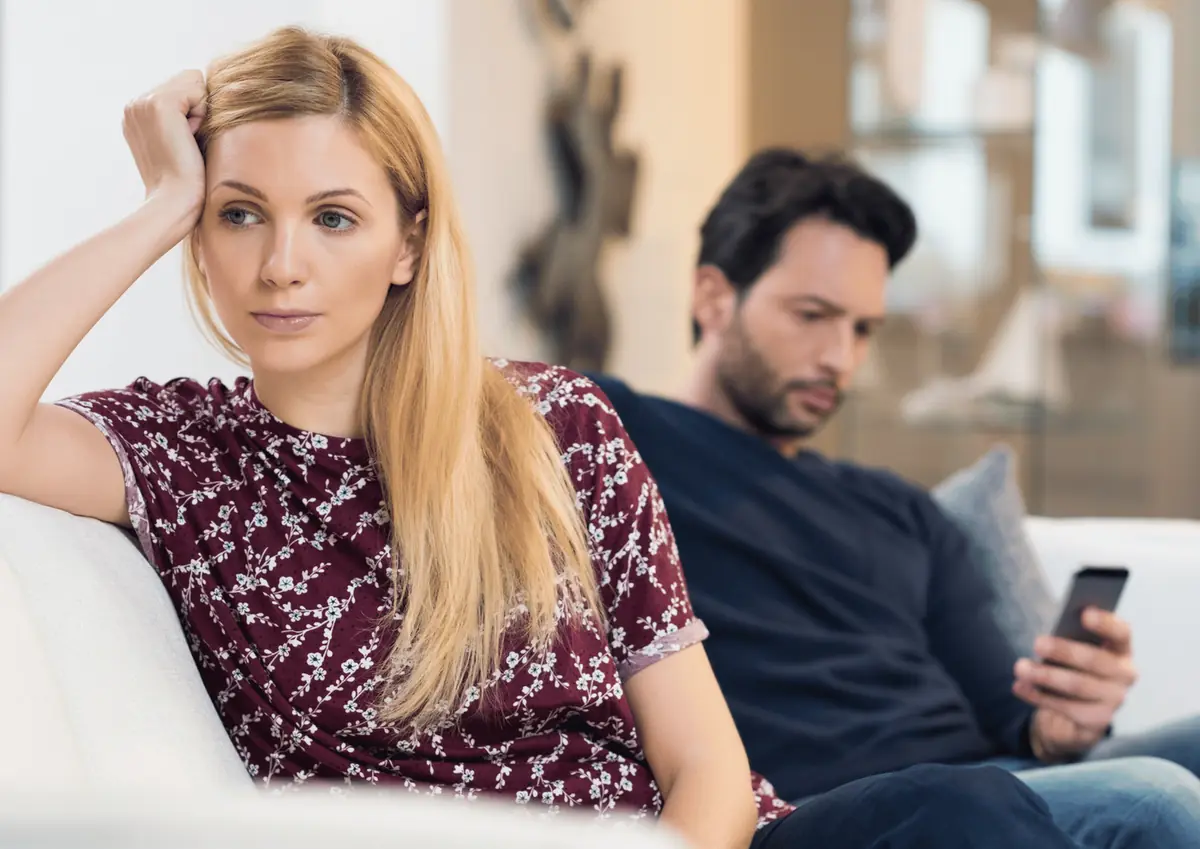 Bored wife on the couch while her husband looks at his phone